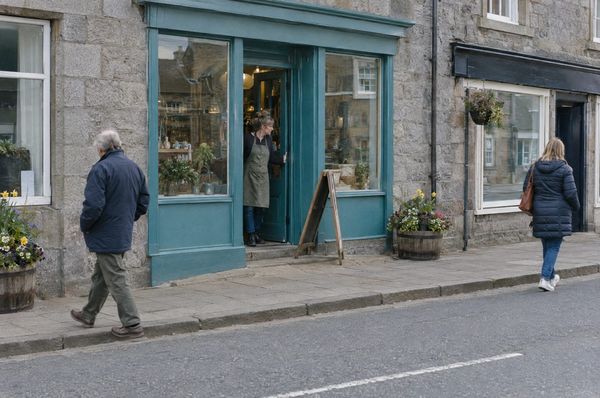 A shop owner opening her teal shop door on a stone high street in a Moray town