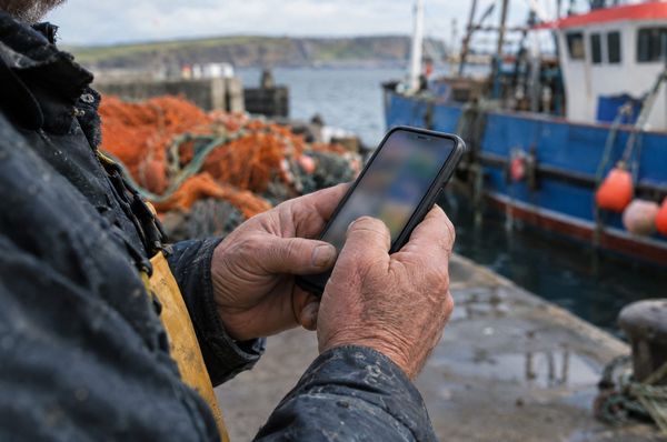 A fisherman scrolling on his phone on the pier at a Moray harbour